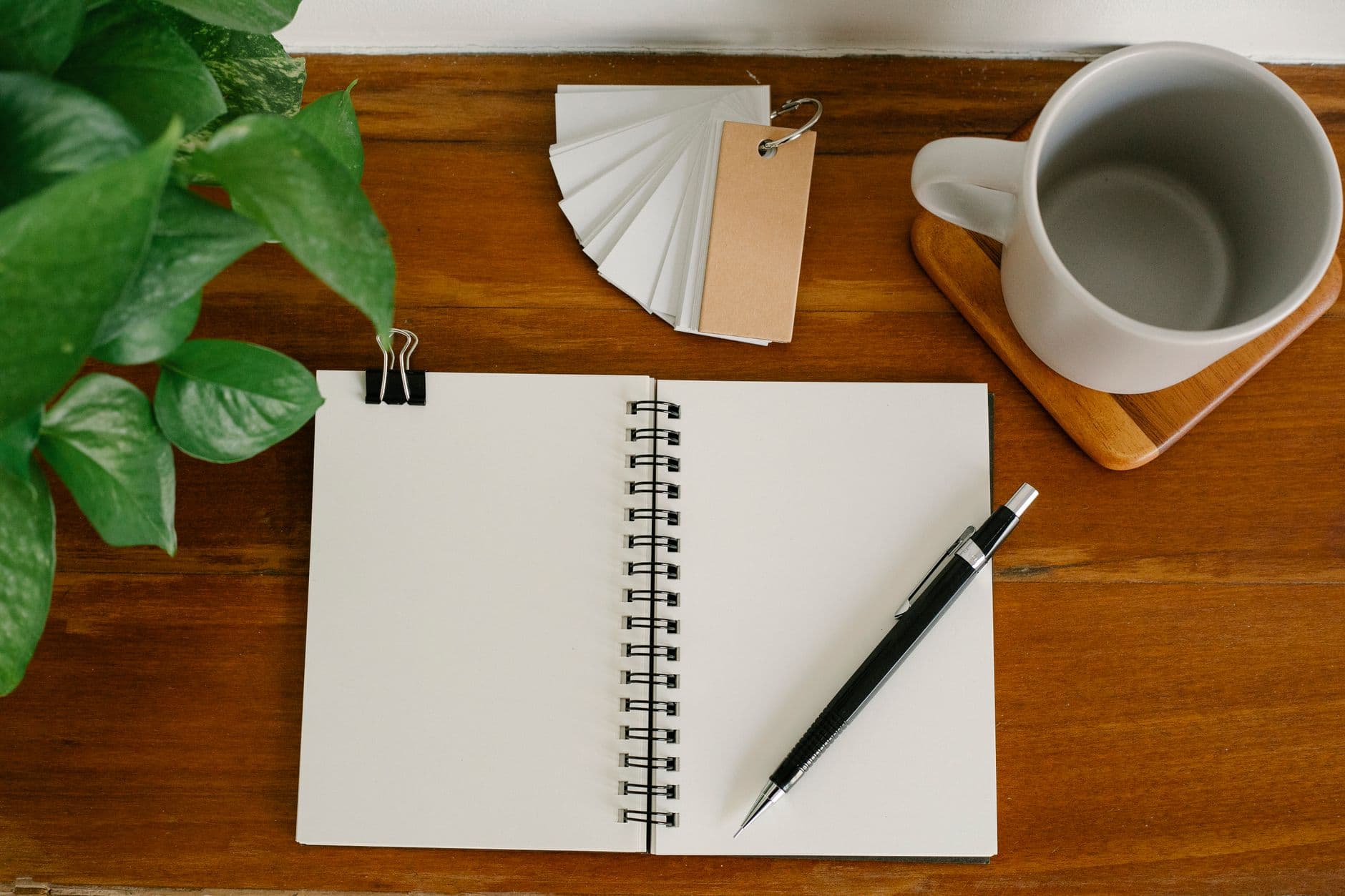 Libreta abierta con lápiz, taza y planta sobre un escritorio de madera